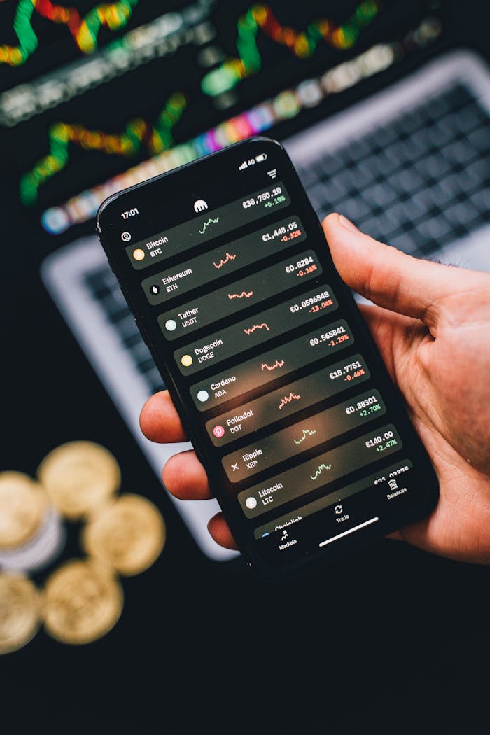 Hand holding phone showing cryptocurrency trends with coins in the background.